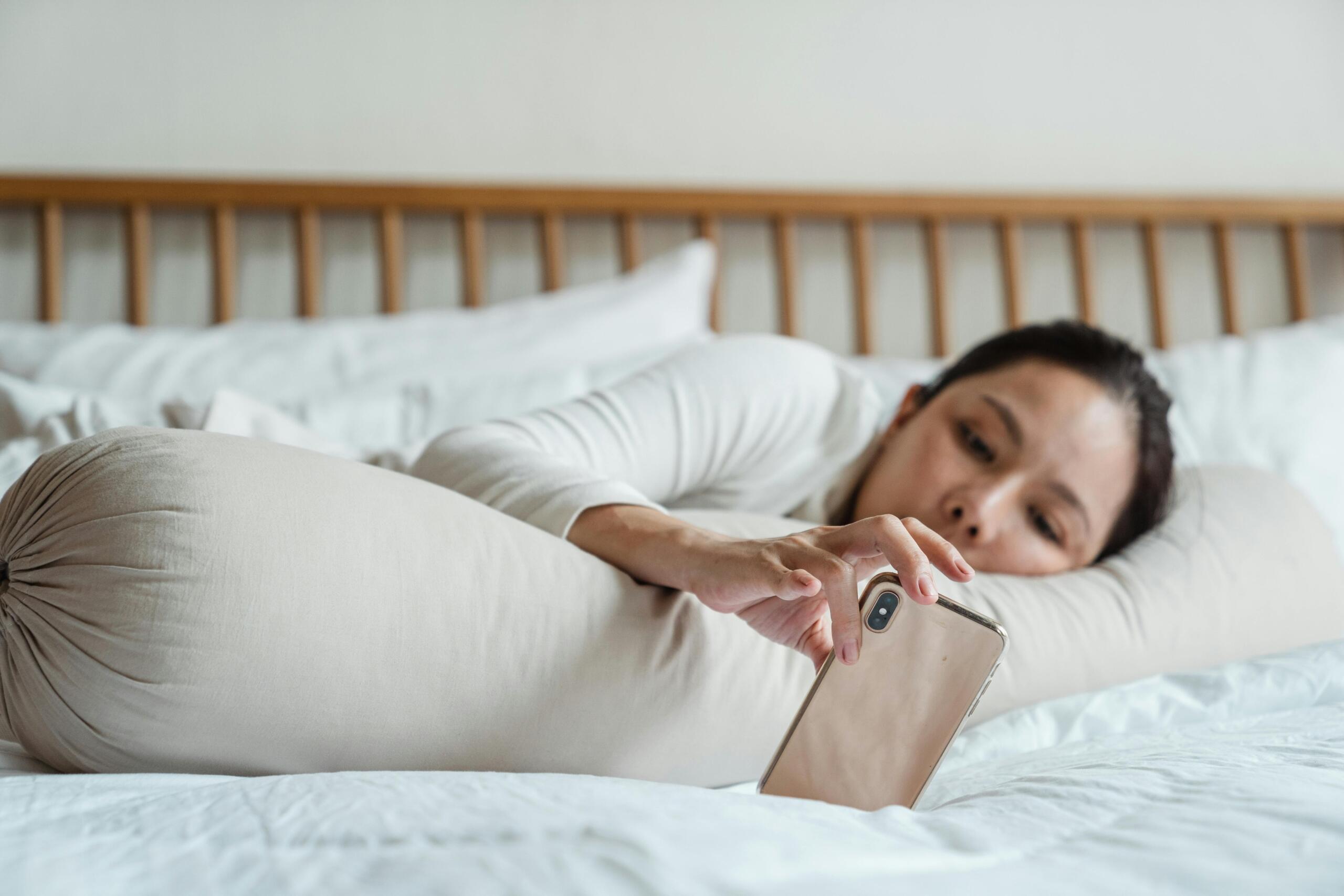 A young girl scrolling on her phone in bed.