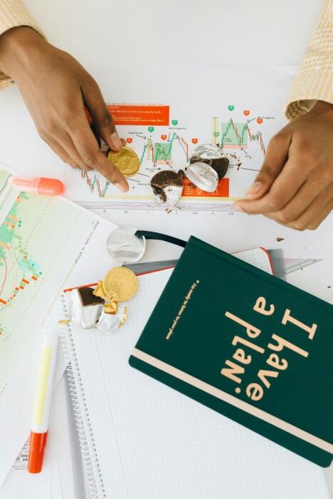 Mains d'une personne ouvrant une pièce en chocolat sur des feuilles représentant des graphiques et un carnet marqué "I have a plan"