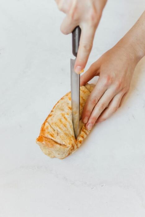 Photo d'un wrap avec des mains le coupant en deux à l'aide d'un couteau